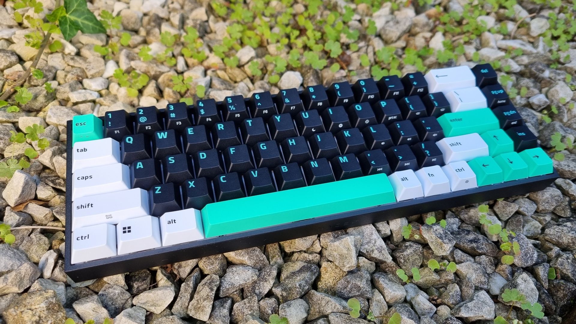A Razer Reclusa X Mini 65% gaming keyboard on top of gravel